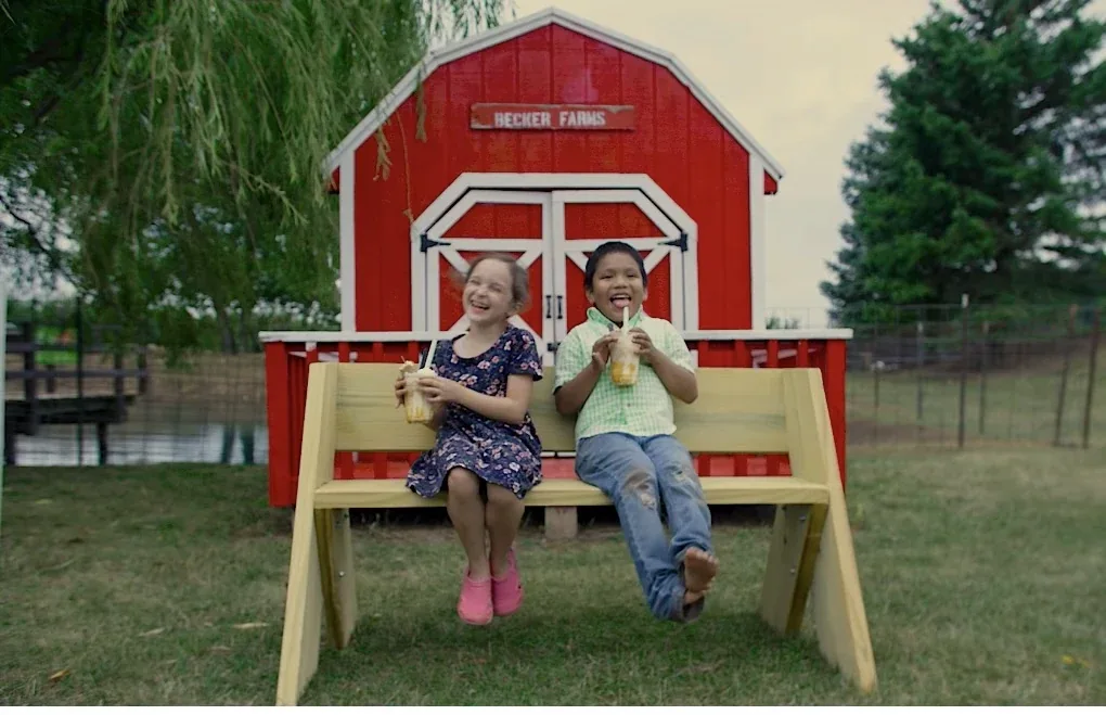 Children seated beside Becker Farms’ red farmyard barn