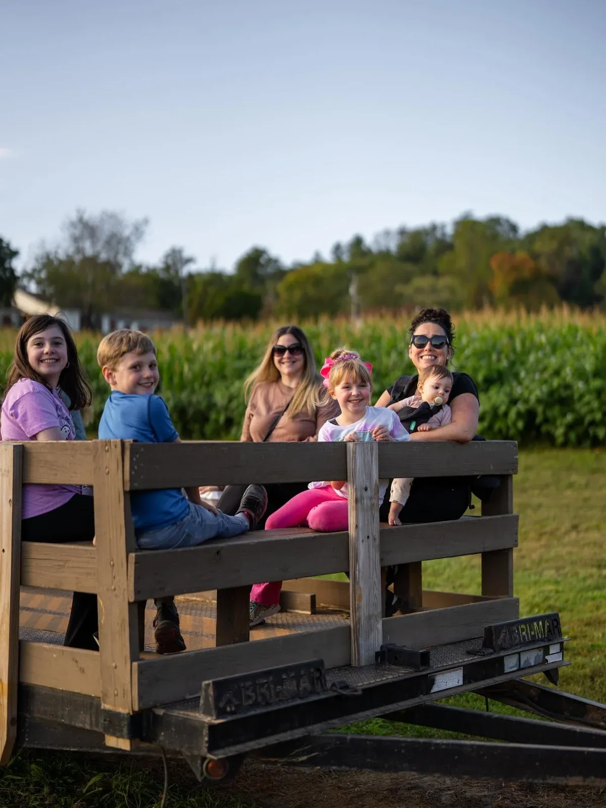 Visitors riding a wooden farm wagon beside corn at Eliada